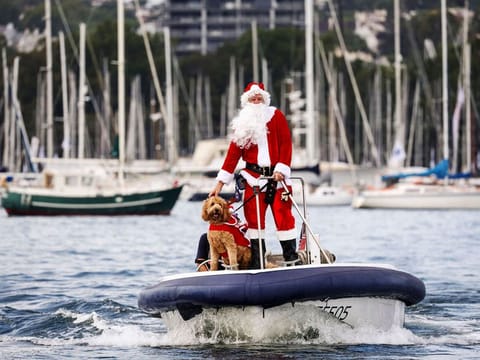 A man dressed as Santa Claus rides a boat with his dog in front of yachts as part of Christmas Day celebrations for the annual Sydney to Hobart yacht race on December 25, 2023. 