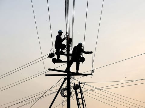 Technicians are silhouetted as they fix cables on a power transmission line in Karachi, Pakistan 