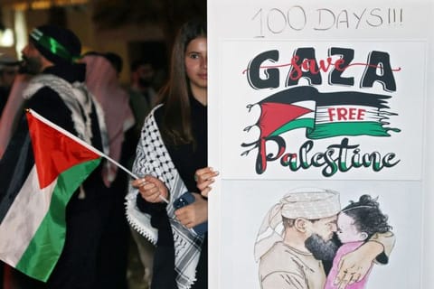 A Kuwaiti woman wearing the traditional Palestinian keffiyeh waves a Palestinian flag as she stands behind a placard during a rally in solidarity with the people of Gaza at Iradah Square in Kuwait City on January 14, 2024.