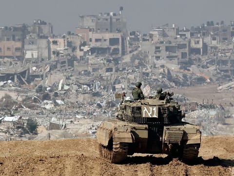 A picture taken from a position in southern Israel along the border with the Gaza Strip on January 19, 2024, shows an Israeli tank rolling along the fence as damaged buildings are see in the Gaza strip amid continuing battles between Israel and the militant group Hamas. 