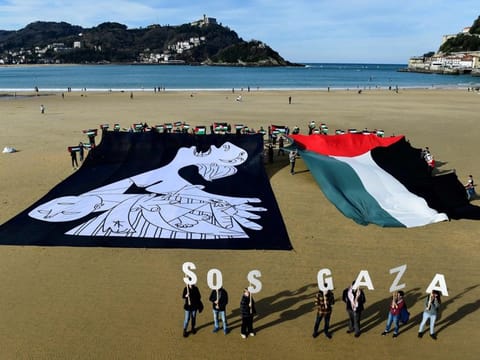 Demonstrators hold a canvas with a detail of Spanish painter Pablo Picasso's masterpiece "Guernica" depicting a mother, and wave a giant Palestinian flag during a protest in solidarity with the Palestinian people under the slogan "SOS Gaza", on La Concha beach in the Spanish Basque city of San Sebastian on January 28, 2024.  