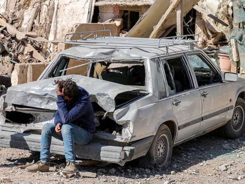 A youth sits by a damaged vehicle outside a destroyed building in the aftermath of an overnight Israeli airstrike on the city of Baalbek in east central Lebanon on March 12, 2024.  