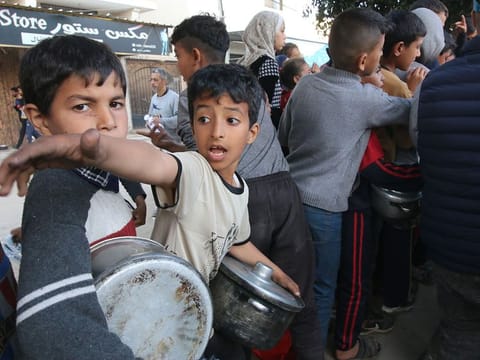 Displaced Palestinian children wait to collect free food handouts from a street kitchen in Deir Al Balah, central Gaza