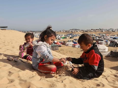 Palestinian children play on a sand dune overlooking a camp for displaced people in Rafah in the southern Gaza Strip on March 17, 2024.