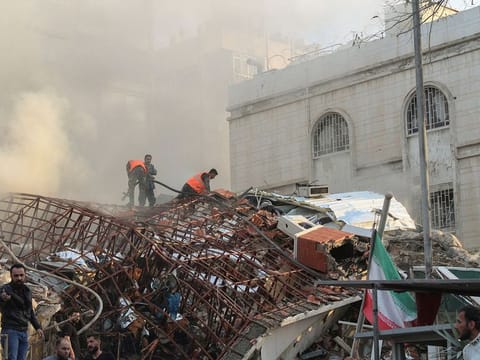 Members of the civil defence stand near a damaged site after an Israeli air strike on Iran's consulate in the Syrian capital Damascus.