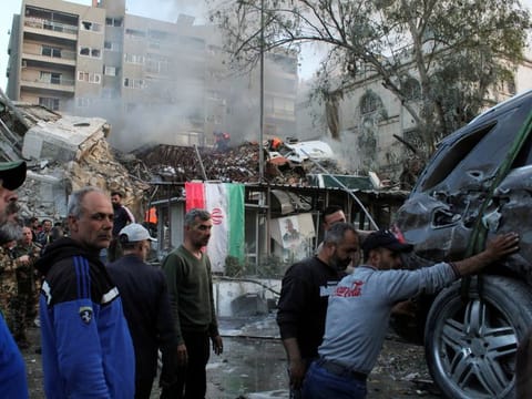 People gather near a damaged site, hauling a destroyed vehicle away, after what Syrian and Iranian media described as an Israeli air strike on Iran's embassy in the Syrian capital Damascus on April 1, 2024.  