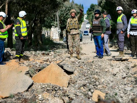 A Lebanese army soldier gestures while holding a wireless transceiver as he stands with other civil defence first responders before an impact crater following an Israeli air strike that hit a road in Lebanon's southern village of Alma Al Shaab on April 15, 2024 amid ongoing cross-border tensions.