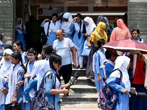 Students leaving their school compound carry umbrellas on a hot summer day in Dhaka