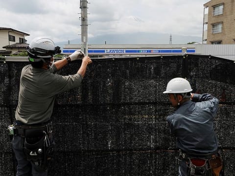 Workers erect a barrier to block the view of a popular Mount Fuji photo spot, near a convenience store in Fujikawaguchiko town, Yamanashi prefecture, Japan, on May 21, 2024.   