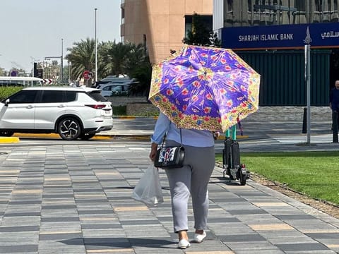 A UAE resident walks holding an umbrella on a hot, sunny day in Abu Dhabi
