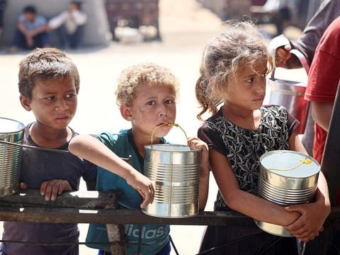 Children wait for food being distributed at a camp for internally displaced people where they live due to the Israeli bombardment of the Gaza Strip, in Khan Yunis, in the southern Gaza Strip on June 11, 2024. 