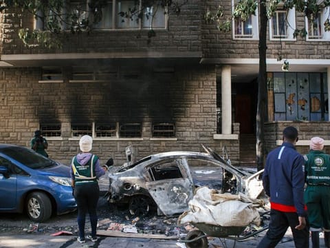 City cleaners look at a burnt-out vehicle following anti-government protests in the Central Business District in Nairobi, Kenya, on Wednesday, June 26, 2024.  