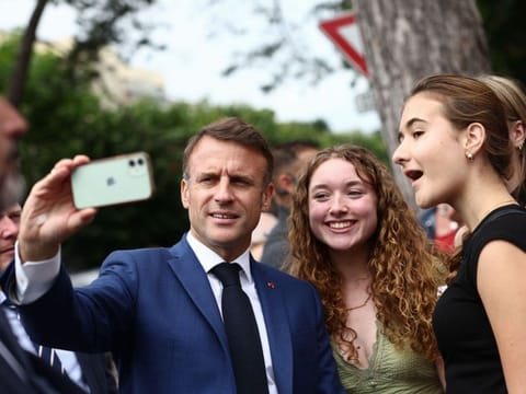 French President Emmanuel Macron takes a selfie as he meets with supporters after voting in the first round of parliamentary elections outside a polling station in Le Touquet, northern France on June 30, 2024.  