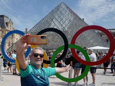 A visitor mades a selfie in front of the Olympic rings placed at Louvre Pyramid.