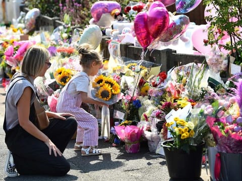 A mother looks at her child laying a bouquet of sunflowers next to floral tributes for the victims of a deadly knife attack in Southport, northwest England, on July 31, 2024.  