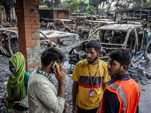 Students gather and discuss in front of some police vehicles that were burned during anti-government demonstrations while waiting at a police station to file complains as students volunteering to maintain law and order are in control of the Jatrabari Police Station in Dhaka on August 11, 2024.  