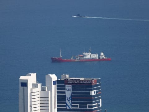 An Israeli submarine (back) is pictured passing behind a ship in the Mediterranean sea off the coast of the northern Israeli city of Haifa on August 12, 2024, as regional tensions rise amid the ongoing war between Israel and the Palestinian Hamas movement in the Gaza Strip.  