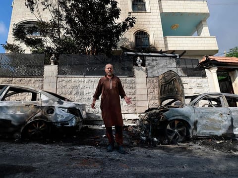 A man stands in front of burnt cars, a day after an attack by Jewish settlers on the village of Jit near Nablus in the occupied West Bank that left a 23-year-old man dead and others with critical gunshot wounds, on August 16, 2024.  