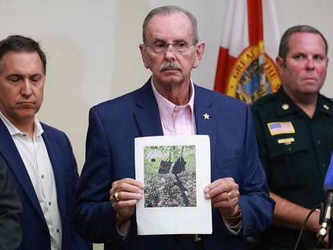 Palm Beach County Sheriff Ric Bradshaw holds a photograph of the rifle and other items found near where a suspect was discovered during a press conference.
