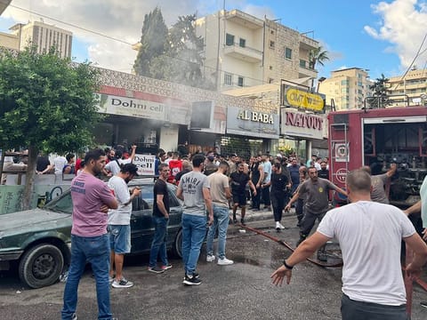 People gather as fire fighters put out the fames at the scene of a reported device explosion in Saida in southern Lebanon on September 18, 2024. 