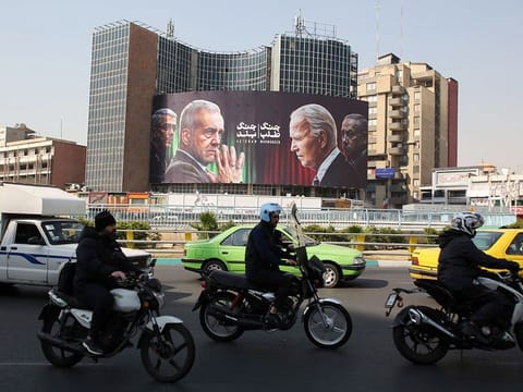 Commuters drive past a billboard bearing pictures of Iran's President Masoud Pezeshkian (2-L), armed forces chief of staff Major General Mohammad Bagheri (L) US President Joe Biden (2-R) and Israeli Prime Minister Benjamin Netanyahu (R) in Vali-Asr square in Tehran on October 27, 2024.   