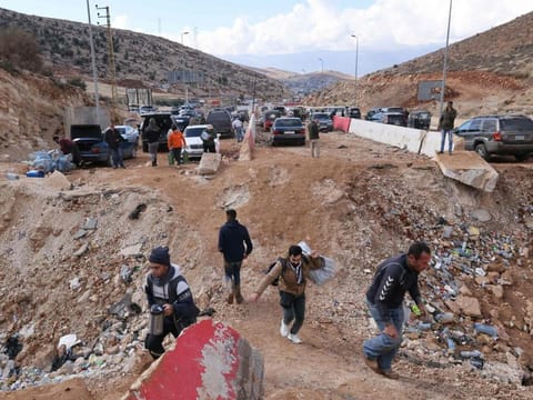 People fleeing Israeli bombardment in Lebanon cross a crater, caused by an Israeli strike, in the area of Masnaa on the Lebanese side of the border crossing with Syria, on November 20, 2024.  