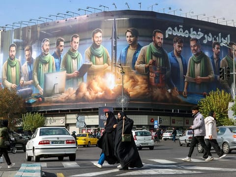 People walk past an anti-Israel billboard that reads in Farsi, "Iran on the frontline", covering the facade of a building in central Tehran. 