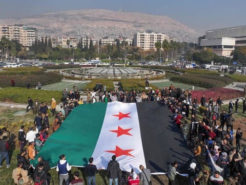 People hold a large Syrian opposition flag at Umayyad Square in Damascus on December 9, 2024.  