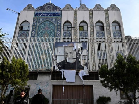 Syrian men stand outside the building of the Iranian embassy which was ransacked after Syrian rebels took Damascus the previous day, with a portrait of Iran's slain Revolutionary Guards commander Qasem Soleimani, still hanging on its fence in the Syrian capital on December 9, 2024.  
