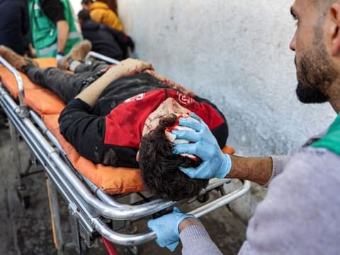 Palestinian Red Crescent paramedics transport on a gurney a person who was injured in a reported strike on a Palestinian civilian vehicle by Israeli forces, after arriving for medical care at the Ahli Arab Hospital in Gaza City on December 22, 2024.